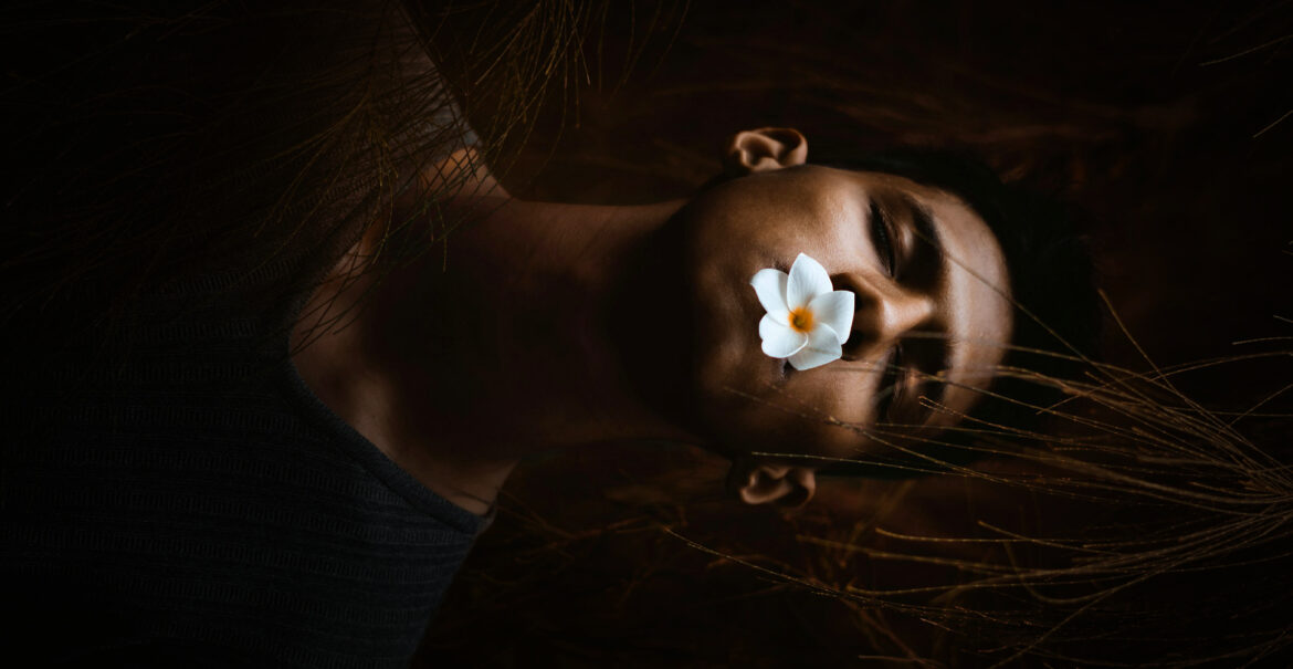 man with eyes closed and a flower in mouth depicting death or being asleep.