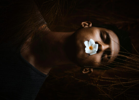 man with eyes closed and a flower in mouth depicting death or being asleep.