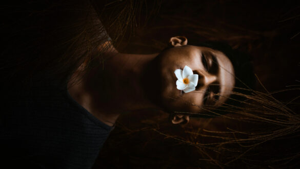 man with eyes closed and a flower in mouth depicting death or being asleep.