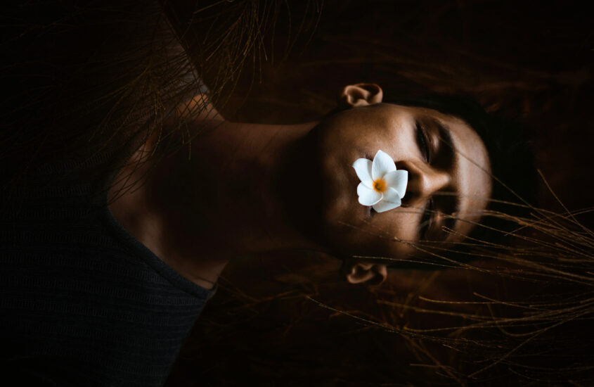 man with eyes closed and a flower in mouth depicting death or being asleep.